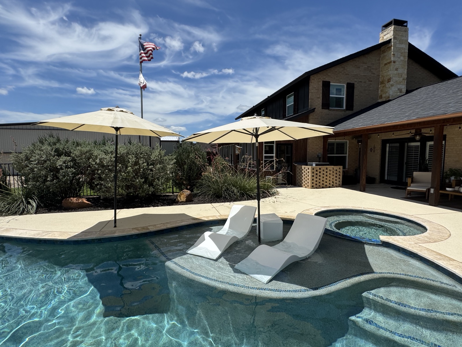 Pool midday with in-pool chaise loungers and American and Texas flags