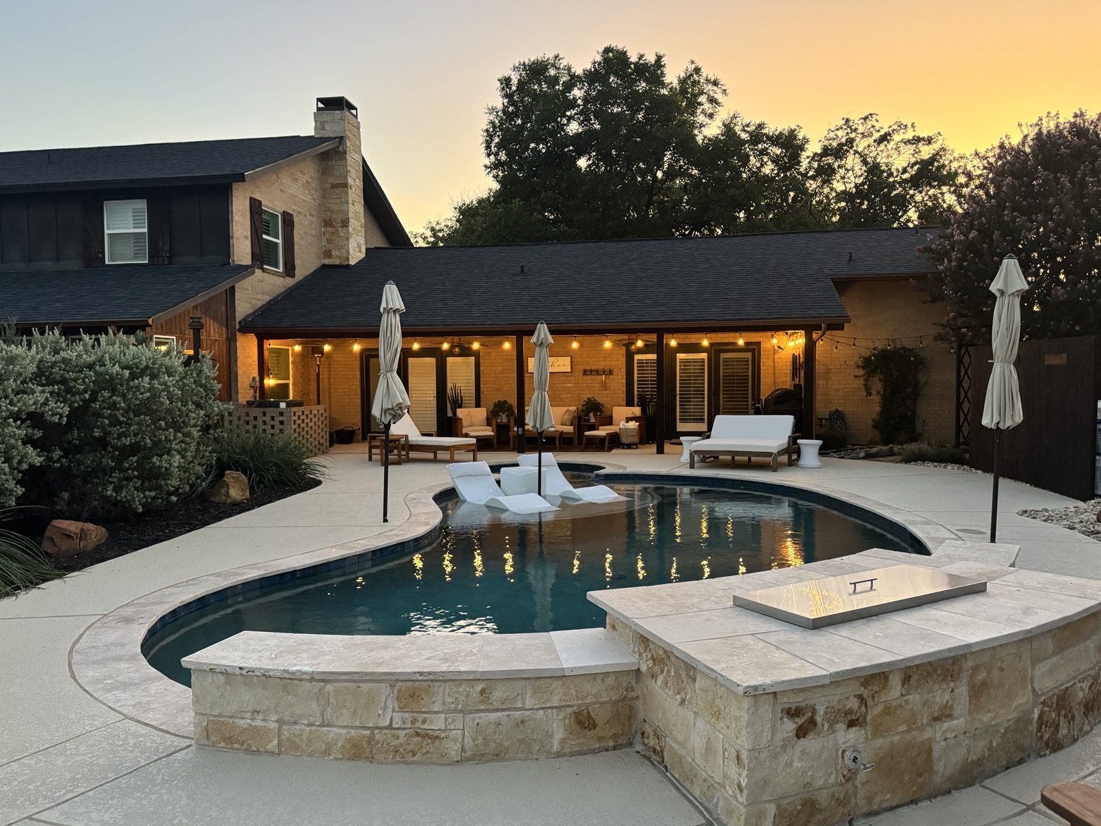 Pool at golden hour with fire table lit, covered porch string lights glowing warm